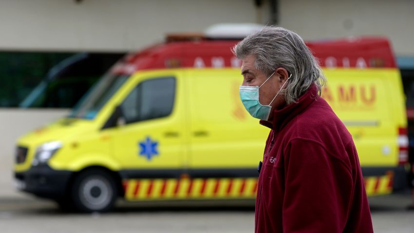 A man wearing a face mask walks past an ambulance outside La Fe hospital on March 25, 2020, in Valencia. - Spain has signed a multi-million-euro contract with China to acquire medical supplies to fight the coronavirus epidemic, the health minister said today. Worth some 432 million euros ($467 million), the deal will cover 550 million masks, 5.5 million rapid test kits, 950 respirators and 11 million pairs of gloves to address shortages in Spain. The announcement came as Spain saw the number of deaths surge to 3,434 after more than 738 people died in the past 24 hours, overtaking the figure in China where the virus originated late last year. (Photo by Jose Jordan/AFP/Getty Images)