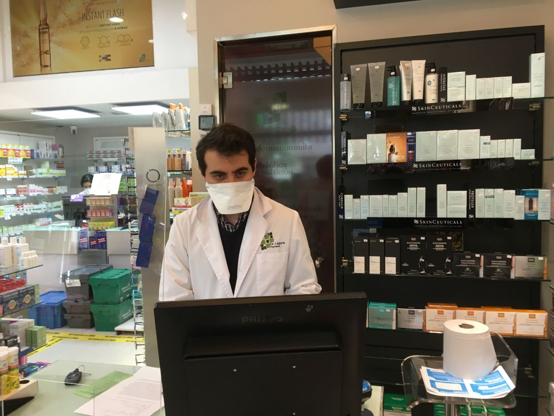 Ernesto Ruiz Lopez stands behind protective screen at counter of his Madrid pharmacy.