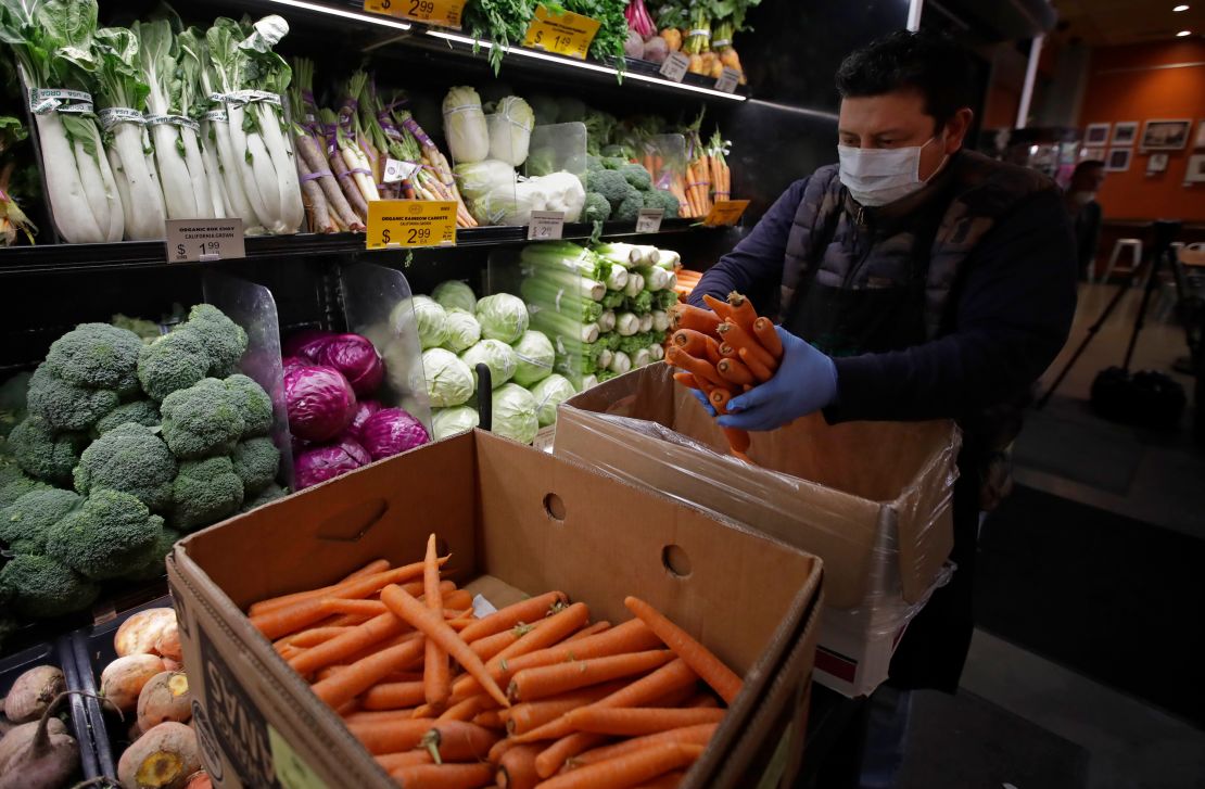A worker, wearing a protective mask against the coronavirus, stocks produce at Gus's Community Market in San Francisco.
