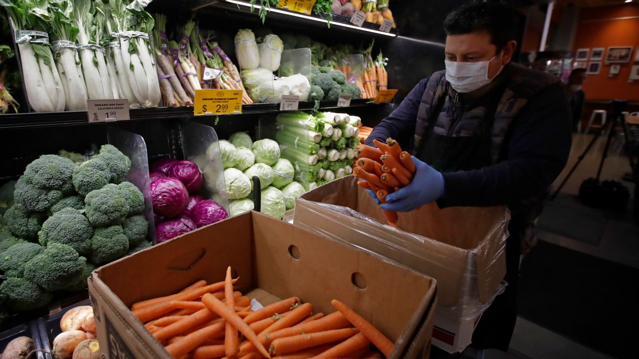 A worker, wearing a protective mask against the coronavirus, stocks produce at Gus's Community Market in San Francisco. 