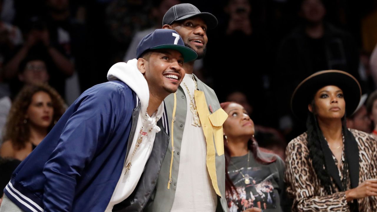 Carmelo Anthony, left, and LeBron James watch Dwyane Wade play in his last NBA game on April 10, 2019, in New York with Gabrielle Union, right.
