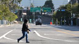 A woman wears a mask as she crosses an empty street near the Los Angeles Convention Center in downtown Los Angeles California March 30, 2020. - The California National Guard is currently setting up the convention center as a field hospital to help lessen the strain on LA-area hospitals during the coronavirus crisis. (Photo by Robyn Beck/AFP/Getty Images)