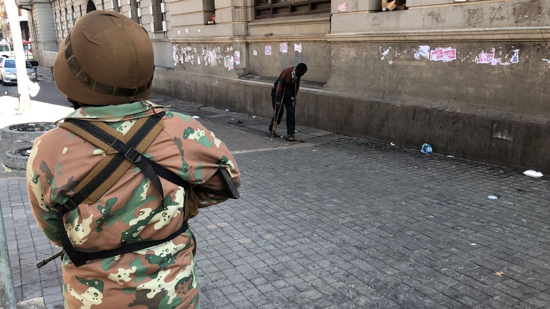 A soldier looks on past a man on crutches during South Africa's lockdown.