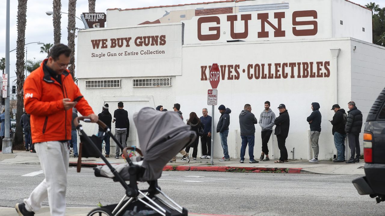 A man walks with a stroller as people stand in line outside the Martin B. Retting, Inc. guns store on March 15, in Culver City, California. The FBI has seen a spike in gun sale background checks amid the coronavirus pandemic.