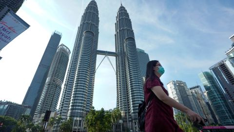 A woman wearing a face mask walks in front of Twin Towers in Kuala Lumpur, Malaysia, on March 18.