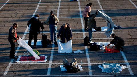 People prepare places to sleep in area marked by painted boxes on the ground of a parking lot at a makeshift camp for the homeless Monday, March 30, 2020, in Las Vegas. 