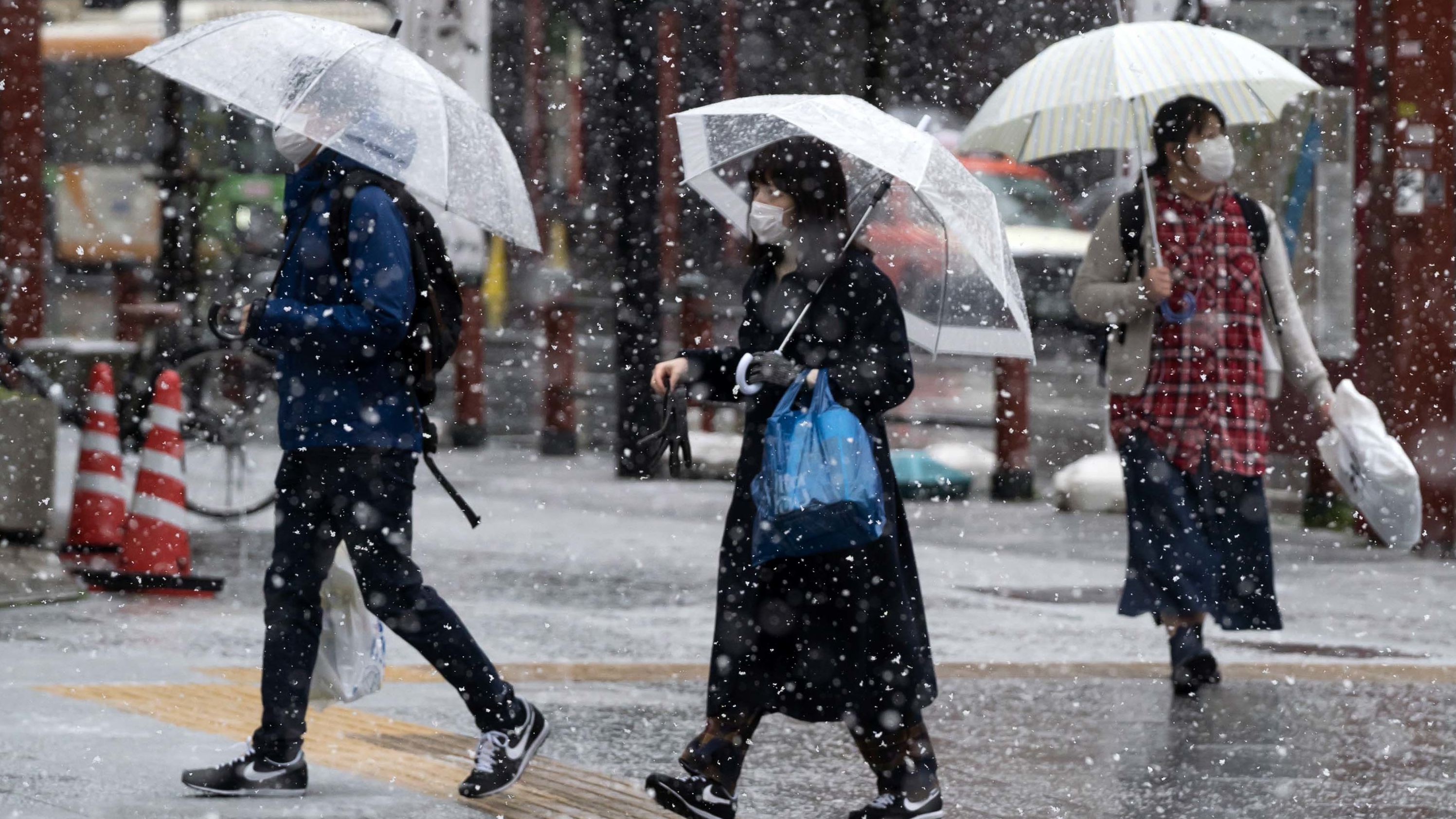 Snow falls as people wearing face masks walk through Tokyo's  Asakusa district on March 29.