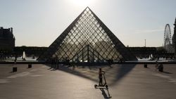 A boy rides an electric scooter in front of the Pyramid of The Louvre Museum (Pyramide du Louvre) as the sun sets in Paris on July 3, 2019. (Photo by Ludovic MARIN / AFP)        (Photo credit should read LUDOVIC MARIN/AFP via Getty Images)