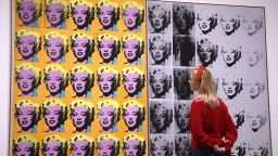 A gallery assistant poses with an artwork entitled "Marilyn Diptych" 1962," by US artist Andy Warhol during a press preview for the Andy Warhol exhibition at the Tate Modern