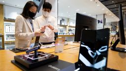 An employee wearing a protective mask, right, assists a customer looking at a Samsung Electronics Co. Galaxy Z Flip smartphone at the company's D'light flagship store in Seoul, South Korea, on Friday, March 6, 2020.
