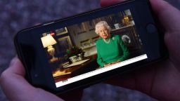 A picture shows a person in Birkenhead, northwest England on April 5, 2020 posing holding a smartphone showing Britain's Queen Elizabeth II deliver a special address to the UK and  Commonwealth recorded at Windsor Castle in relation to the coronavirus outbreak. - Queen Elizabeth II urgeed people to rise to the challenge posed by the coronavirus outbreak, in a rare special address to Britain and Commonwealth nations on Sunday. (Photo by Paul ELLIS / AFP) (Photo by PAUL ELLIS/AFP via Getty Images)