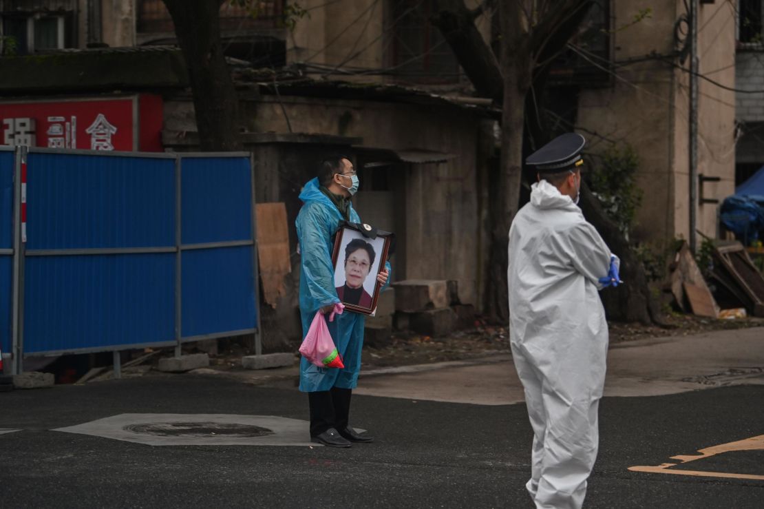 A man wearing a mask and a blue raincoat holds a portrait as he stands outside the Biandanshan cemetery in Wuhan on March 31.