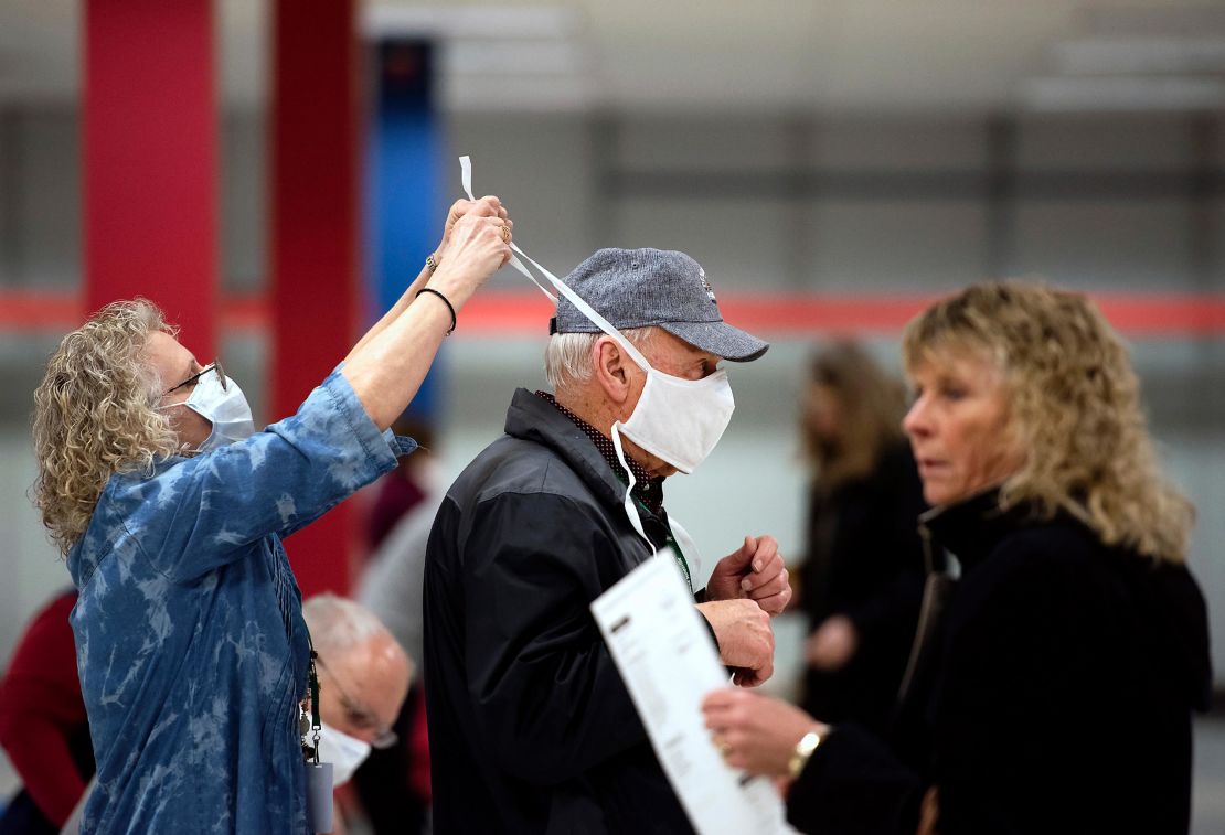 Poll worker Patty Piek-Groth, left, helps fellow poll worker Jerry Moore put on a mask as polls open last Tuesday at the Janesville Mall in Janesville, Wisconsin.