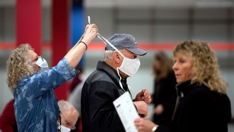 Poll worker Patty Piek-Groth, left, helps fellow poll worker Jerry Moore put on a mask as polls open last Tuesday at the Janesville Mall in Janesville, Wisconsin.