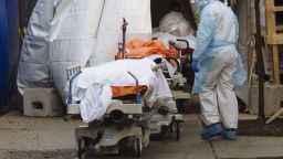 A medical worker in protective clothing walks past the bodies of deceased patients from a refrigerated overflow morgue outside the Wyckoff Heights Medical Center in Brooklyn, New York, U.S., on Friday, April 3, 2020. Officials from New York City began to warn that the health system was nearing its capacity to handle the waves of patients, with possibly just days to go before reaching the limits of ventilators and hospital bed space. Photographer: Angus Mordant/Bloomberg via Getty Images
