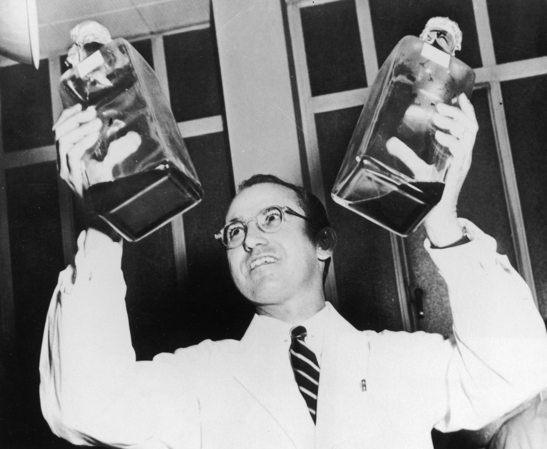 Jonas Salk holds up two decanters containing the anti-polio vaccine that he developed. 