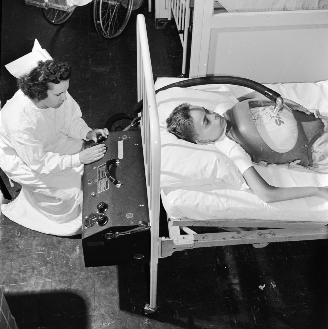 A boy suffering from polio is treated with an "iron lung" at a hospital in 1955, while a nurse controls the flow of air pressure. 