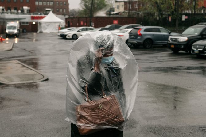 A woman covers herself with plastic as heavy rain falls outside a New York hospital on April 13, 2020.
