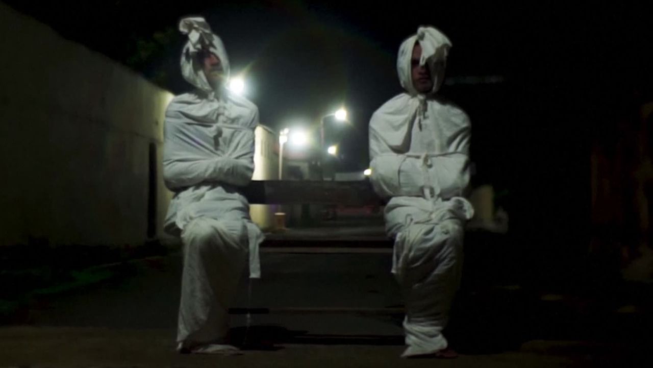 Volunteers Deri Setyawan, 25, and Septian Febriyanto, 26, sit on a bench as they play the role of 'pocong', or known as 'shroud ghost', to make people stay at home amid the spread of coronavirus disease (COVID-19), outside the gate of Kepuh village in Sukoharjo regency, Central Java province, Indonesia, April 1, 2020. Picture taken April 1, 2020. REUTERS/Stringer NO RESALES. NO ARCHIVES.