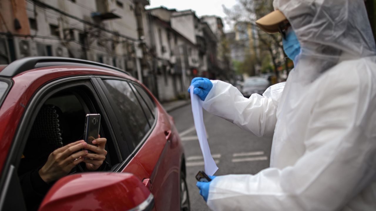 A woman wearing a hazmat suit and face mask holds up a Wuhan city health QR code for residents to scan before entering a residential compound in Wuhan.