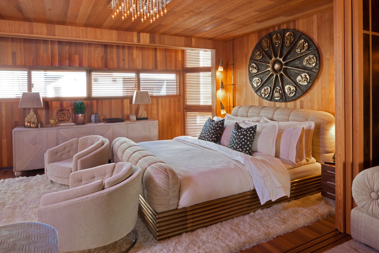 Wearstler designed this guest bedroom for a client's home to feel as if it were on a boat. The walls and ceiling are covered in honey toned teak wood, giving warmth and texture to the space. A 1970s zodiac sculpture above the bed is reminiscent of a starfish.