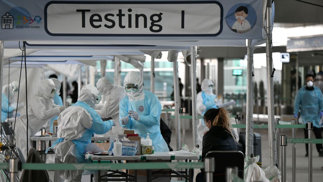 Medical staff wearing protective clothing take test samples for the Covid-19 coronavirus from a foreign passenger at a virus testing booth outside Incheon international airport, west of Seoul, on April 1, 2020.