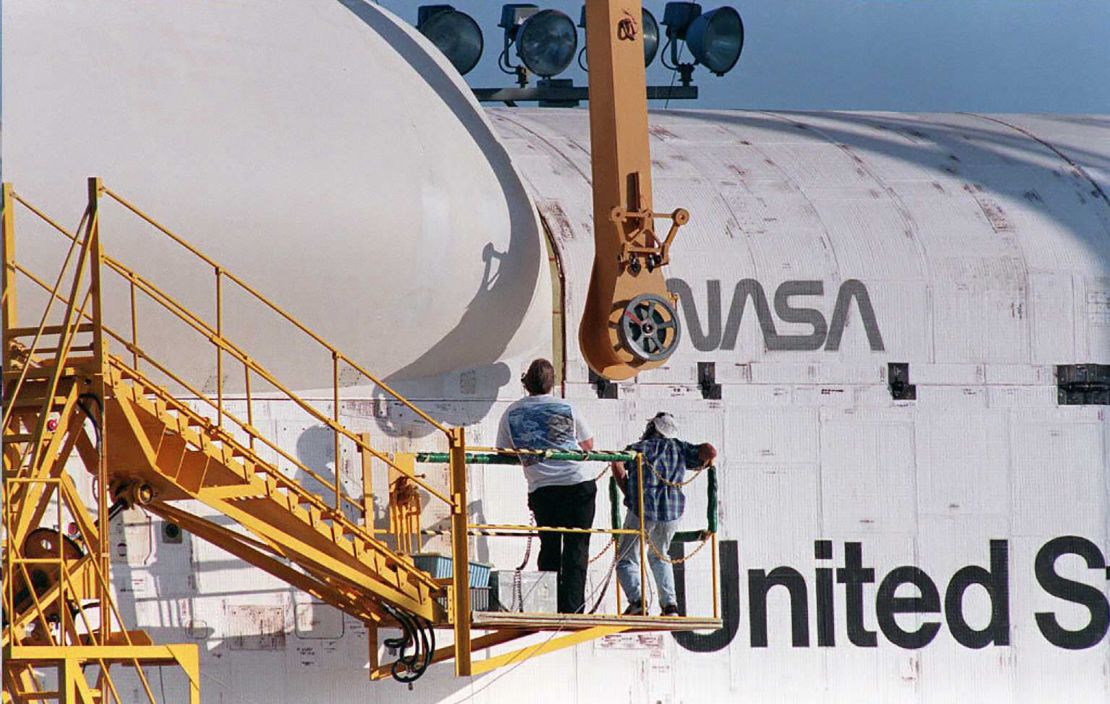 NASA technicians prepare to attach part of a lifting sling to the right rear of the Space Shuttle Discovery