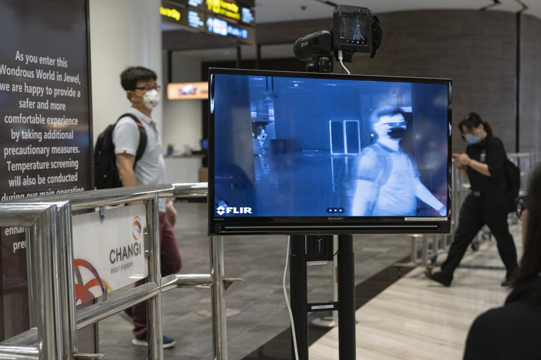 People wearing masks walk past a temperature screening area at Terminal 1 of Changi Airport on March 22, 2020 in Singapore.