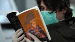 A passenger from Greece with a protective mask reads a book on March 25,2020 at Duesseldorf's airport, western Germany, as the airport remains empty due to the spread of the novel coronavirus COVID-19. - After a decade as Europe's leading disciple of fiscal virtue, Germany is unleashing a flood of government cash to counter the devastating economic impact of the novel coronavirus. Airline group Lufthansa has cancelled almost all flights in the coming weeks, while tour operator TUI has already applied for state aid. (Photo by Ina FASSBENDER / AFP) (Photo by INA FASSBENDER/AFP via Getty Images)