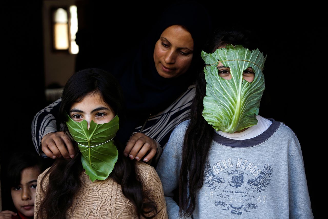 A mother entertains her children with makeshift masks made of cabbage as she cooks in Beit Lahia, Gaza.