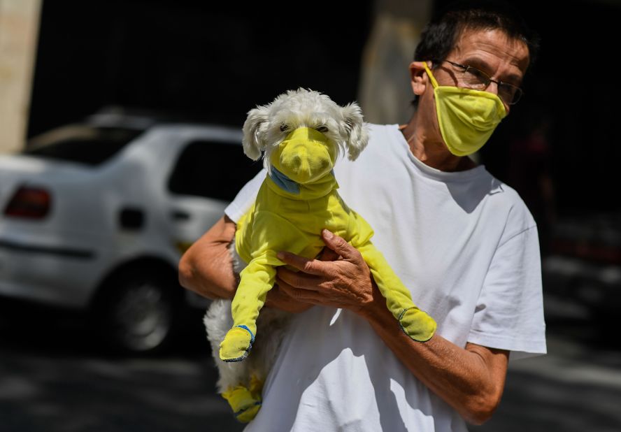 A man in Caracas, Venezuela, wears a face mask while he carries his dog wearing a protective suit.