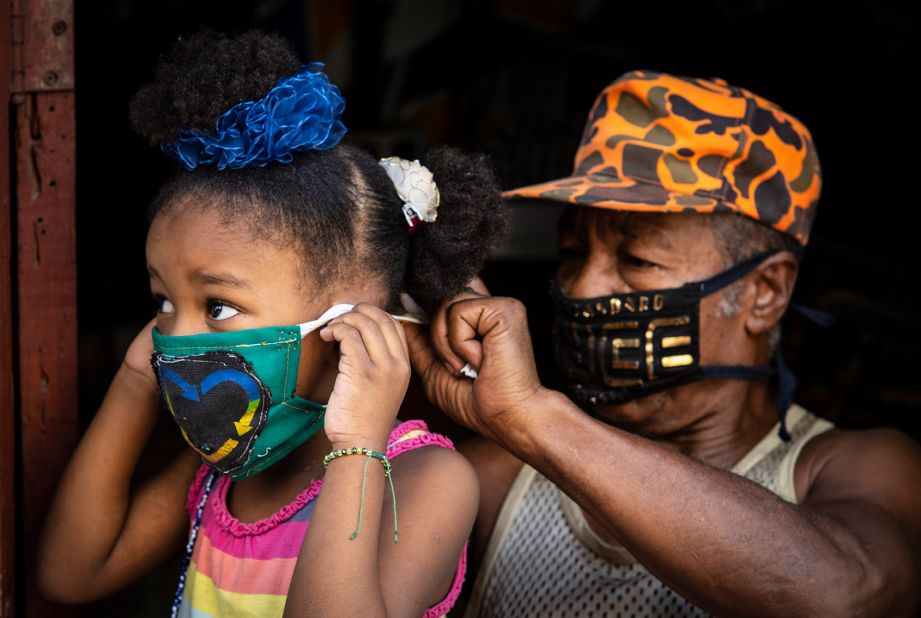 Andres Jimenez, a retired state worker who makes masks to sell in his neighborhood, ties a mask on a girl in Havana, Cuba.