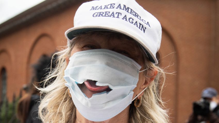 A woman wearing a "Make America Great Again" hat sticks her tongue out of a damaged mask as demonstrators protest during a "Reopen Maryland" rally outside the State House in Annapolis, Maryland, calling on the state to lift stay-at-home orders due to the coronavirus pandemic, April 18, 2020.
