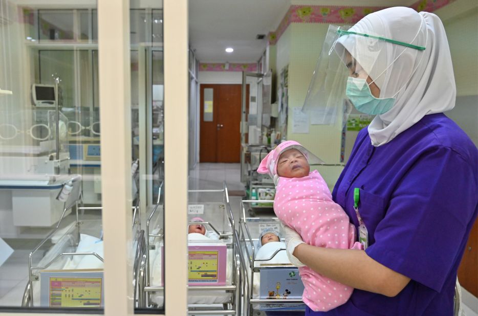 A nurse holds a newborn baby, wearing a face shield as a protective measure, at a maternity facility in Jakarta, Indonesia.