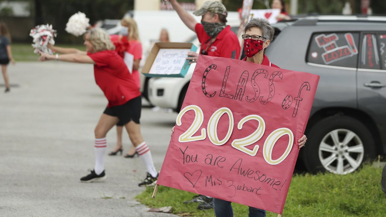 Science teacher Debbie Ziebart, holding sign, cheers with other faculty as graduating seniors receive their caps and gowns in a drive-through parking lot pep rally at Tavares High School in Lake County, Fla. on April 20.