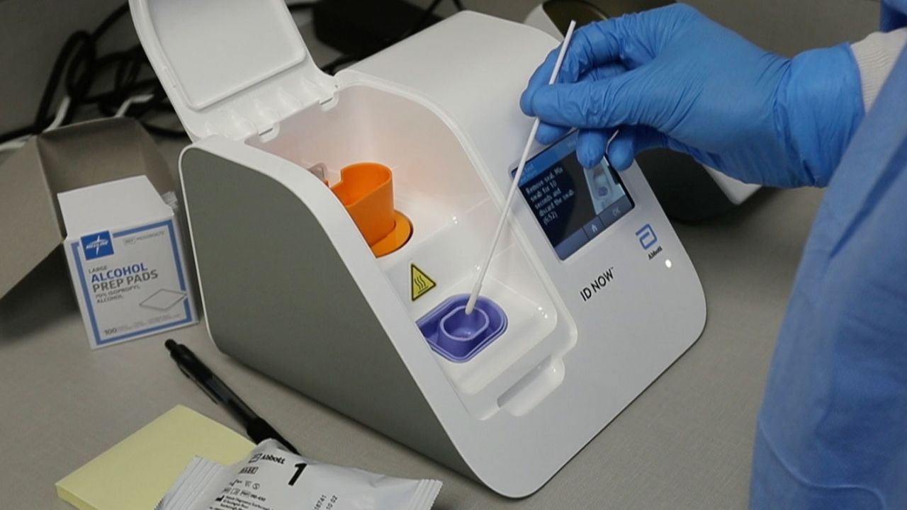FILE - In this April 10, 2020, file frame grab from video, a lab technician dips a sample into the Abbott Laboratories ID Now testing machine at the Detroit Health Center in Detroit. Illinois-based Abbott Laboratories says its cartridge-based test, approved last month, delivers results within minutes. The coronavirus pandemic gave rise to bold promises by President Donald Trump as he led the response in the U.S.  (AP Photo/Carlos Osorio)