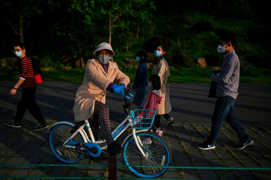 A woman wearing a face mask takes a rest on a bicycle along the East Lake in Wuhan after its lockdown was lifted.