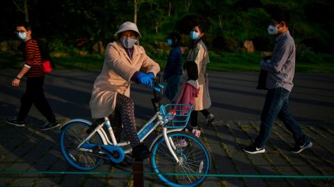 A woman wearing a face mask takes a rest on a bicycle along the East Lake in Wuhan after its lockdown was lifted.