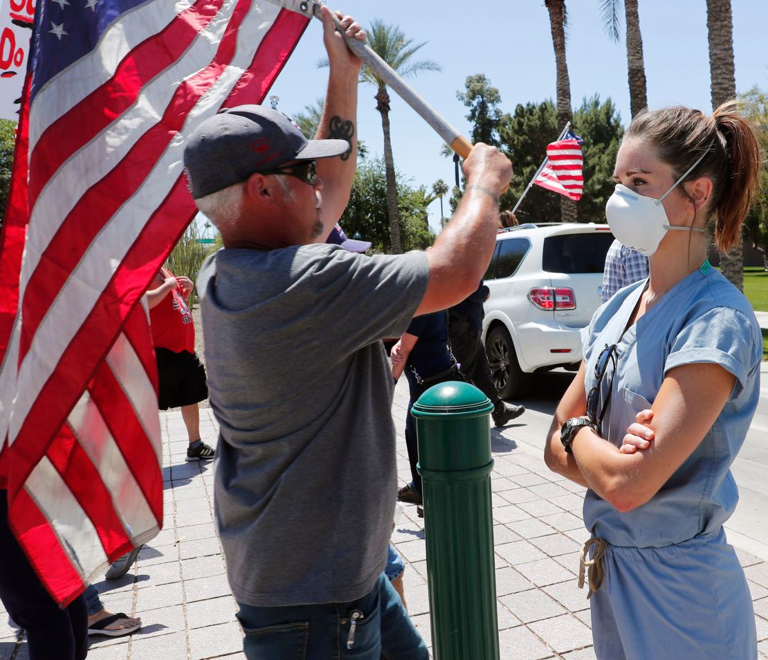 A health care worker stands in counter protest April 20 as people march towards the Arizona state Capitol in protest of Gov. Doug Ducey's stay-at-home order to combat the coronavirus. 