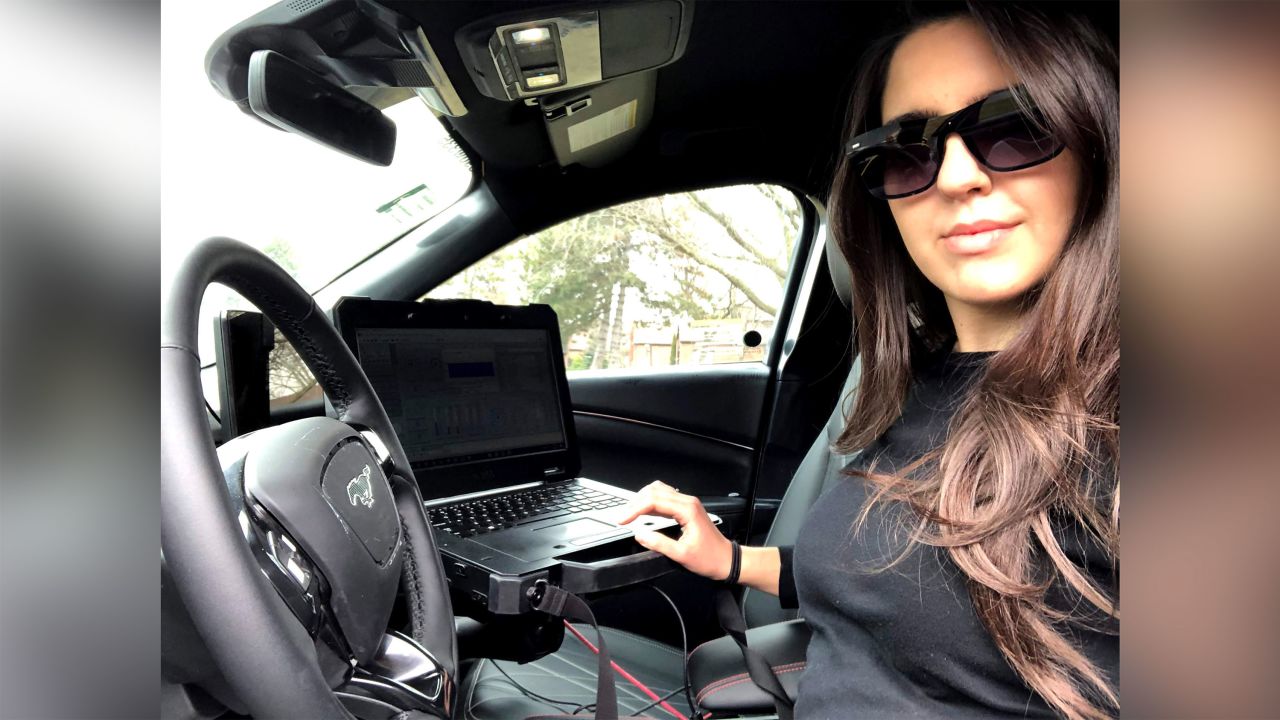 Ford engineer Aleyna Kapur in the driver's seat of a Ford Mustang Mach-E test vehicle with a laptop to record data.