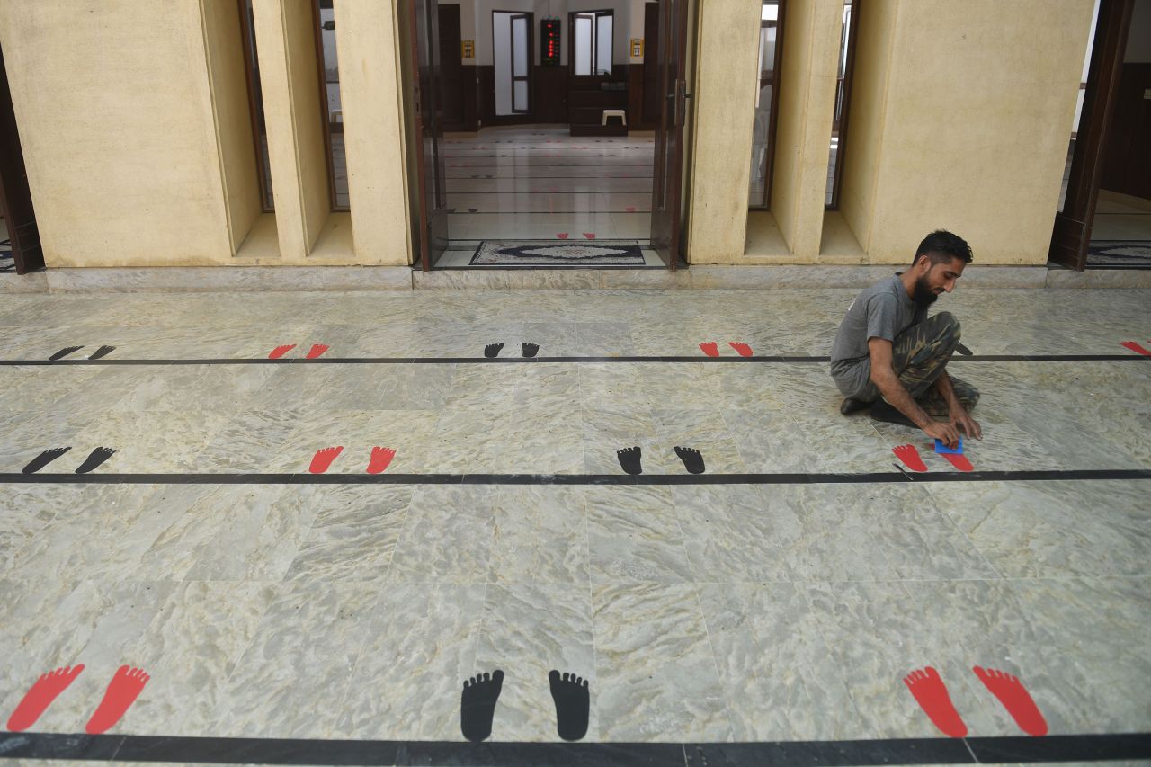 A man in Karachi, Pakistan, places stickers on the floor of a mosque. The idea is to spread people out while they pray.