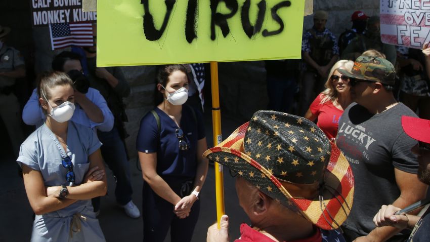Caregivers stand in front of protesters at the main entrance to the Arizona Capitol at a rally to 're-open' Arizona against the governor's stay-at-home order due to the coronavirus Monday, April 20, 2020, in Phoenix. (AP Photo/Ross D. Franklin)