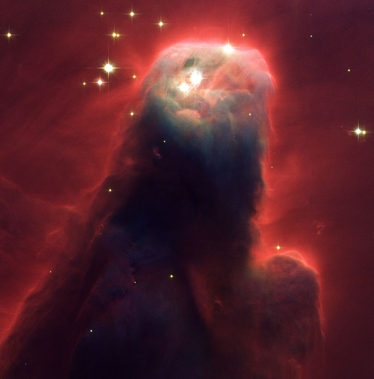 The Cone Nebula is a turbulent star-forming pillar of gas and dust. It's 7 light-years long, but this image taken by Hubble in 2002 shows the top 2.5 light-years (which equals 23 million round trips to the moon). Ultraviolet radiation causes the hydrogen gas to emit an eerie red glow.