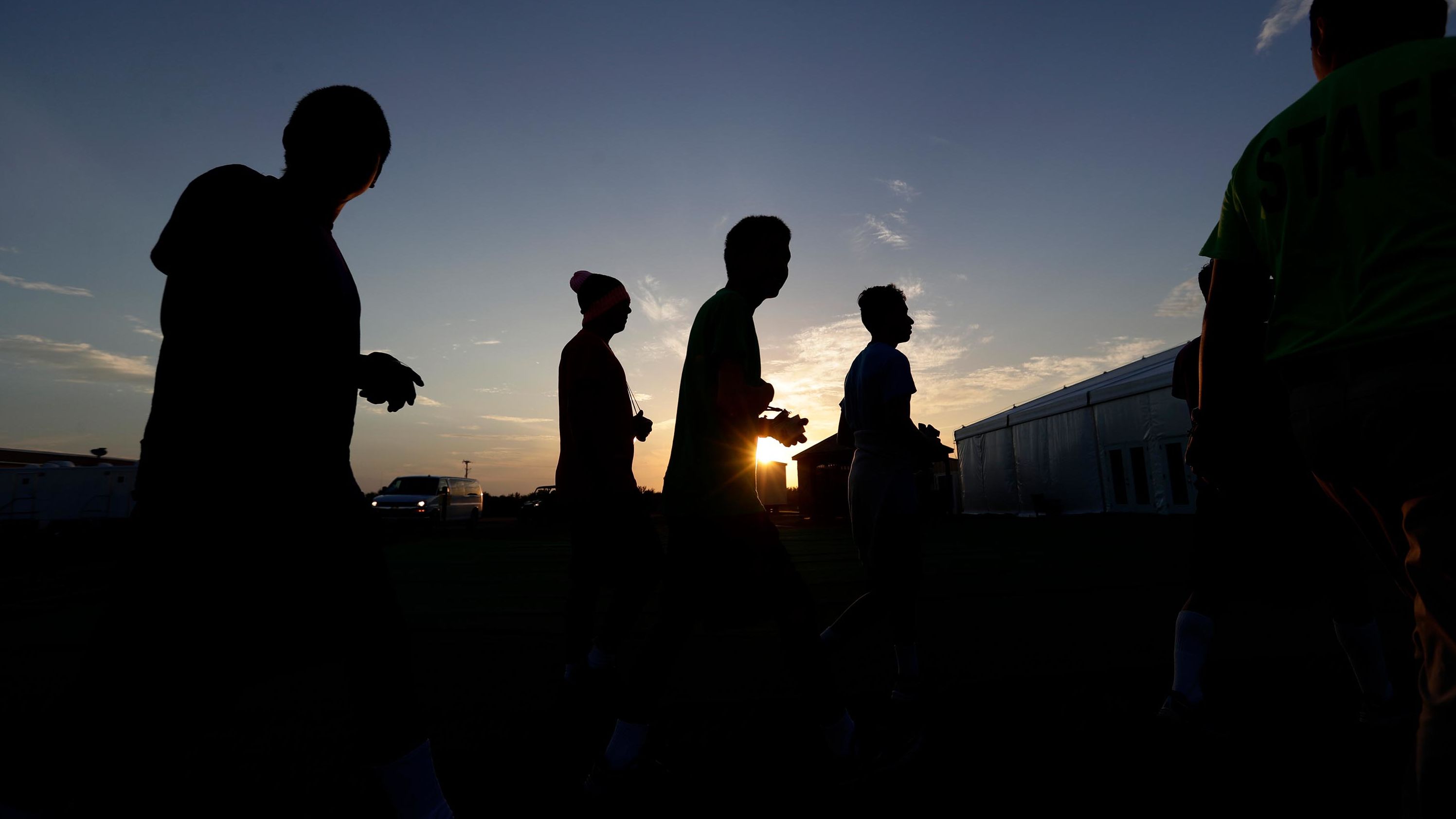 In this July 2019 photo, at sunrise, immigrants are escorted to a tent that serves a dining hall for a U.S. government holding center for migrant children in Texas. 