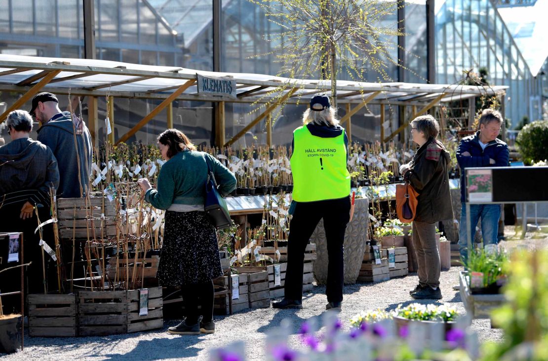 An employee wears a vest reading "Keep distance. Stop Covid-19" as customers look at plants at the Slottstradgarden Ulriksdal garden centre in the Ulriksdal Palace park in Stockholm on April 21.