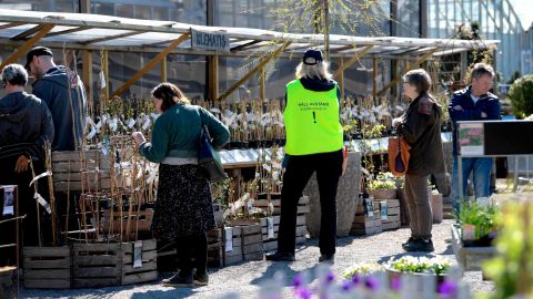 An employee wears a vest reading "Keep distance. Stop Covid-19" as customers look at plants at the Slottstradgarden Ulriksdal garden centre in the Ulriksdal Palace park in Stockholm on April 21.