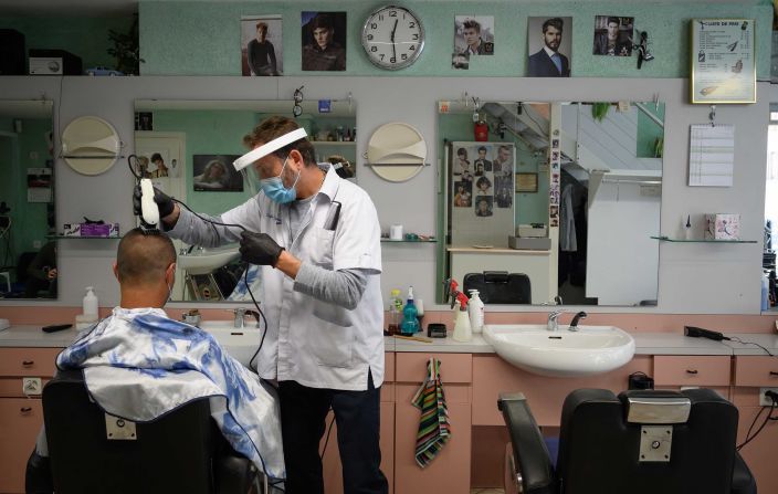 A barber wears protective equipment as he cuts a customer's hair in Lausanne, Switzerland.
