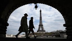 A man and a woman walk on the Bir-Hakeim bridge in front of the Eiffel Tower in Paris on April 2, 2020 on the seventeenth day of a strict lockdown in France to stop the spread of COVID-19 (novel coronavirus). (Photo by Philippe LOPEZ / AFP) (Photo by PHILIPPE LOPEZ/AFP via Getty Images)
