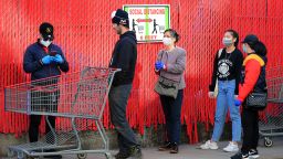 Customers wait in line in front of a sign recommending social distancing to enter the Industry City Costco store on April 28, in the Brooklyn borough of New York City.