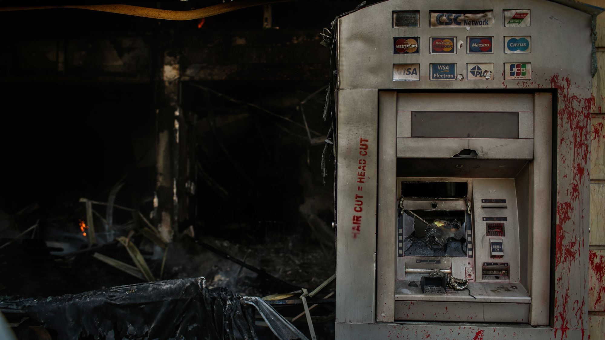 Red paint is seen on a burned ATM on Tuesday. The paint reads "hair cut = head cut."